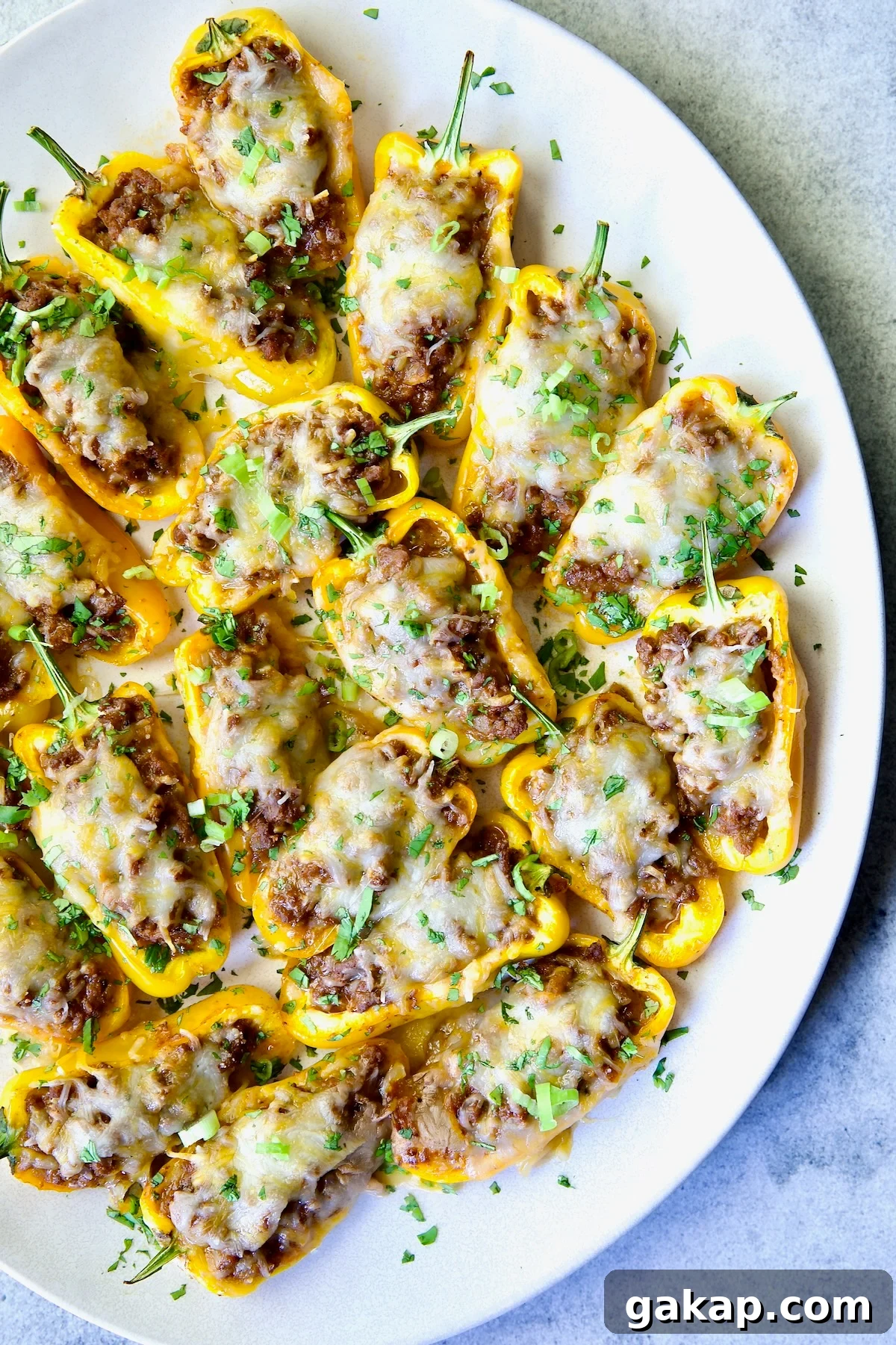 Mini Pepper Tacos: Flavor-Packed Taco-Stuffed Peppers 13 Taco-Stuffed Mini Peppers on white oval platter garnished with thinly sliced scallion and chopped cilantro.