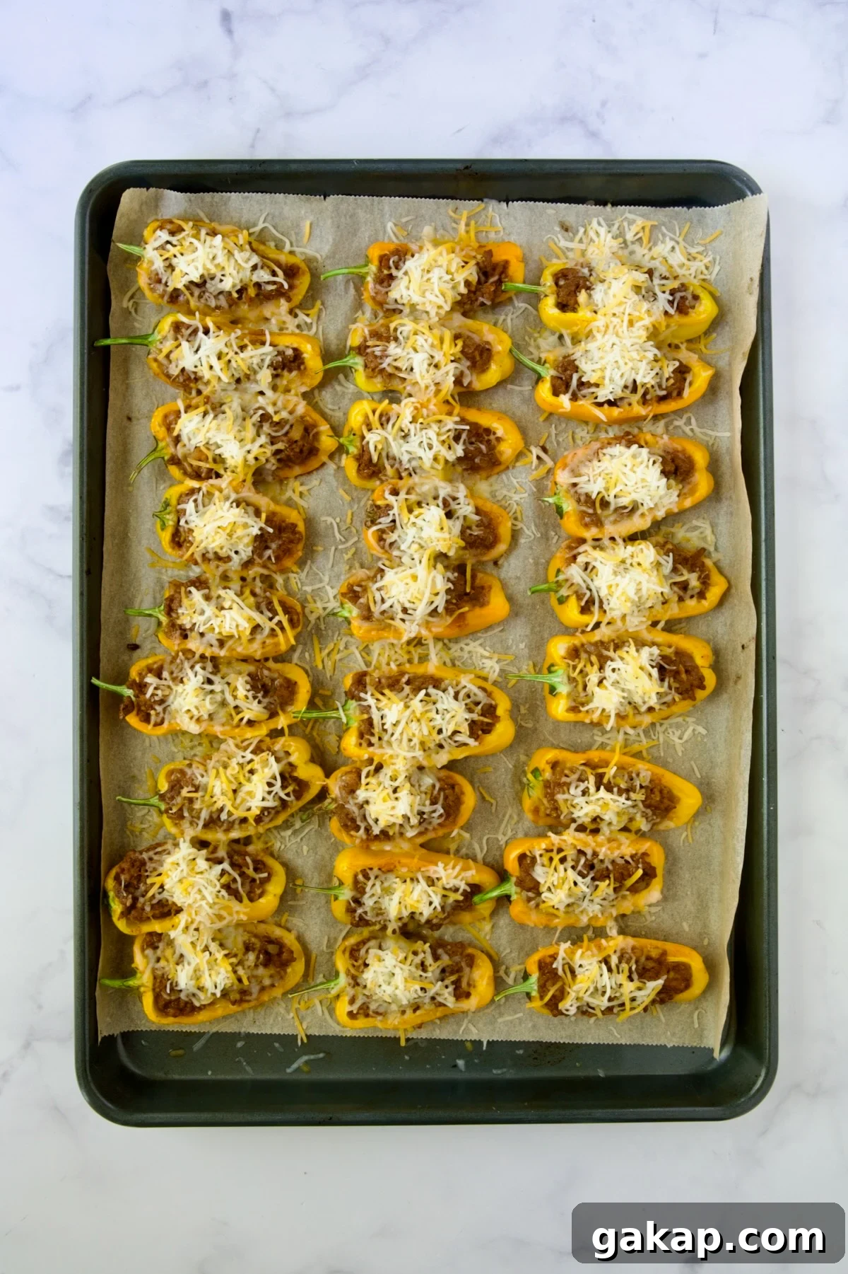 Mini Pepper Tacos: Flavor-Packed Taco-Stuffed Peppers 10 Halved, partially baked yellow mini peppers on parchment paper lined baking sheet with shredded Mexican cheese blend added.
