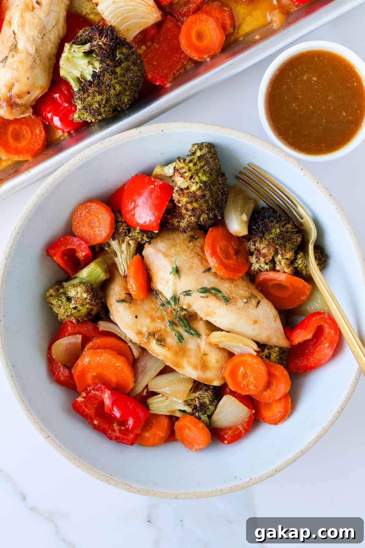 Baked maple chicken and vegges in a bowl with a fork with extra sauce on the side.