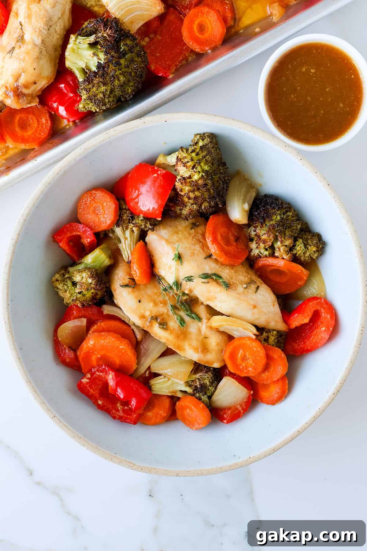 Baked maple chicken and vegges in a bowl with sauce on the side.