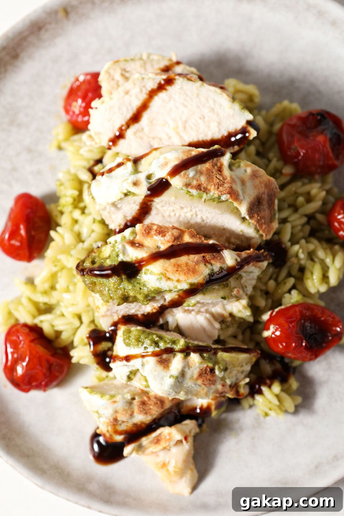 Close up of caprese chicken drizzled with balsamic, served with roasted tomatoes and pesto pasta