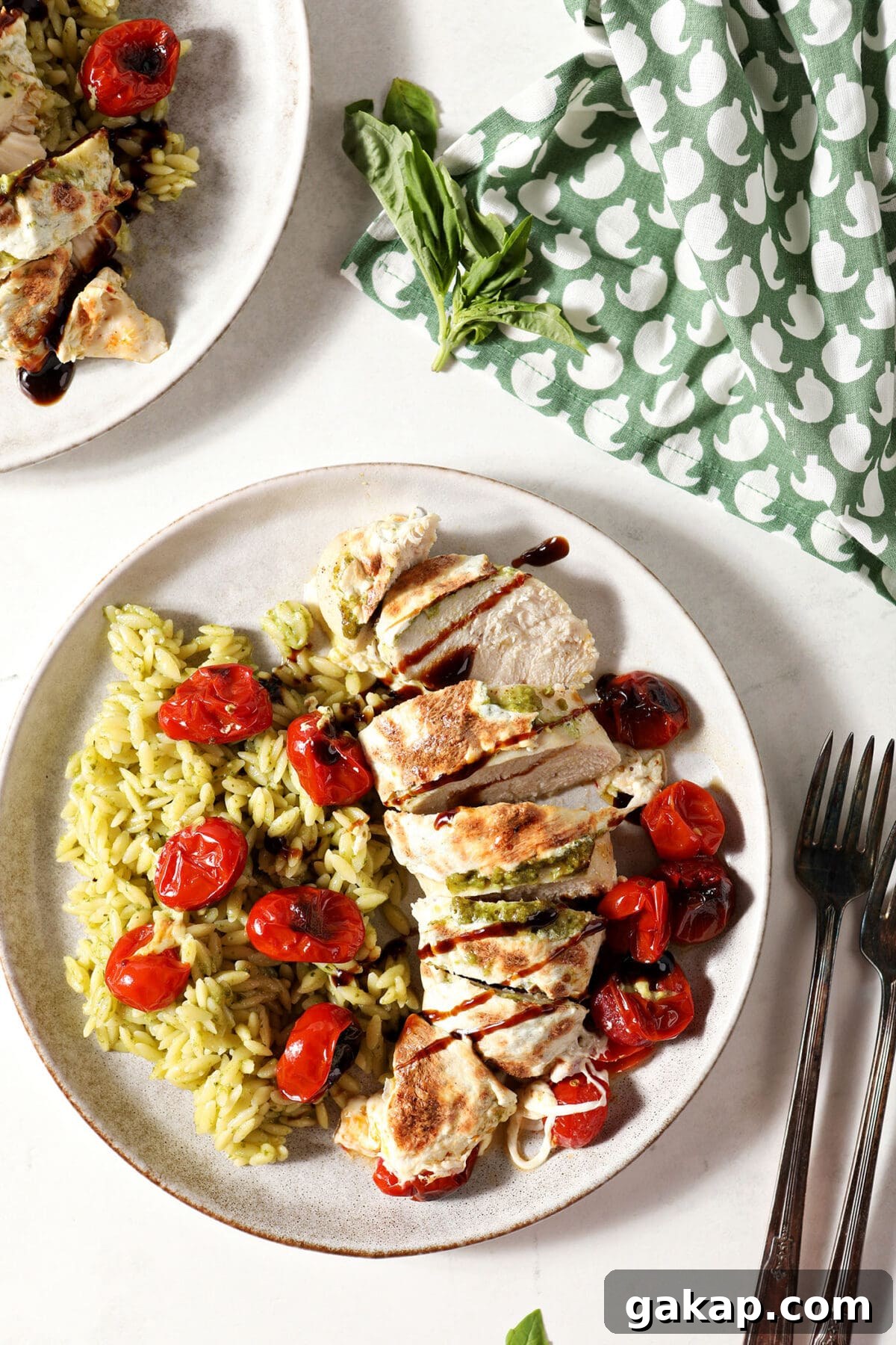 Two plates of baked caprese chicken on a white surface next to a green patterned linen