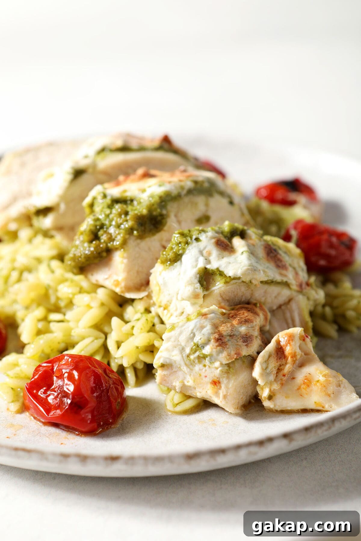 Side view of a sliced caprese chicken breast on top of pesto pasta with roasted tomatoes