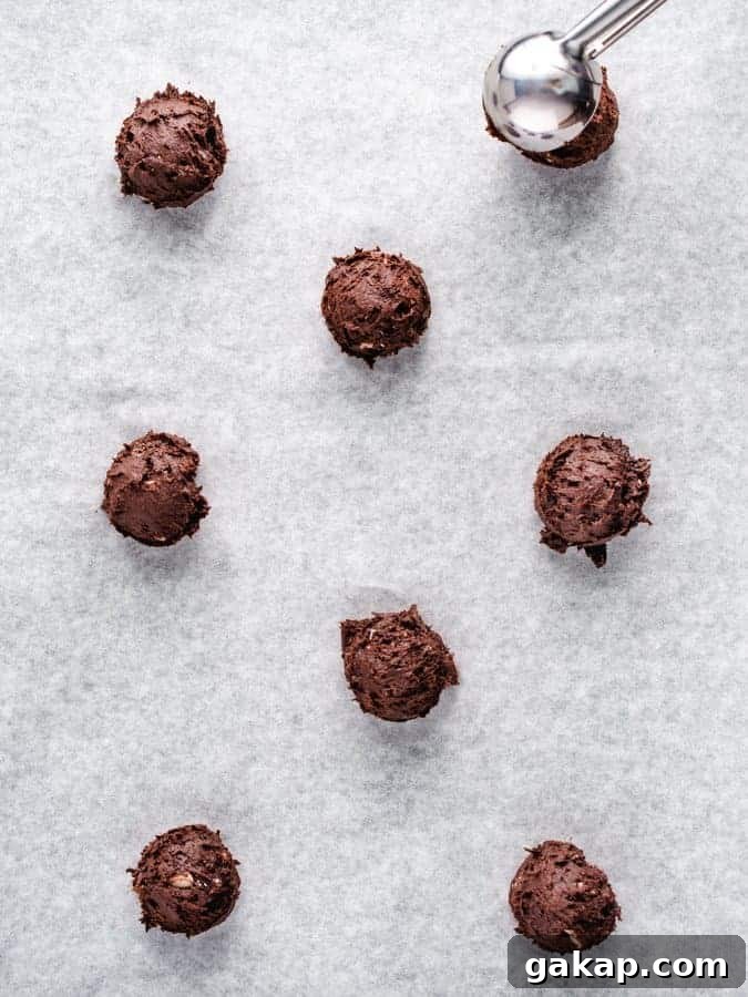 Scooping chocolate peppermint cookie dough onto parchment paper lined baking tray