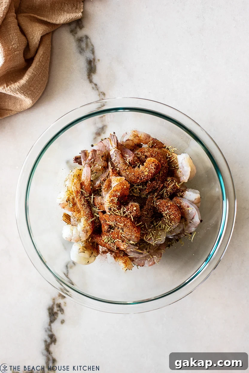 Overhead photo of a glass bowl filled with raw shrimp topped with a spice mixture