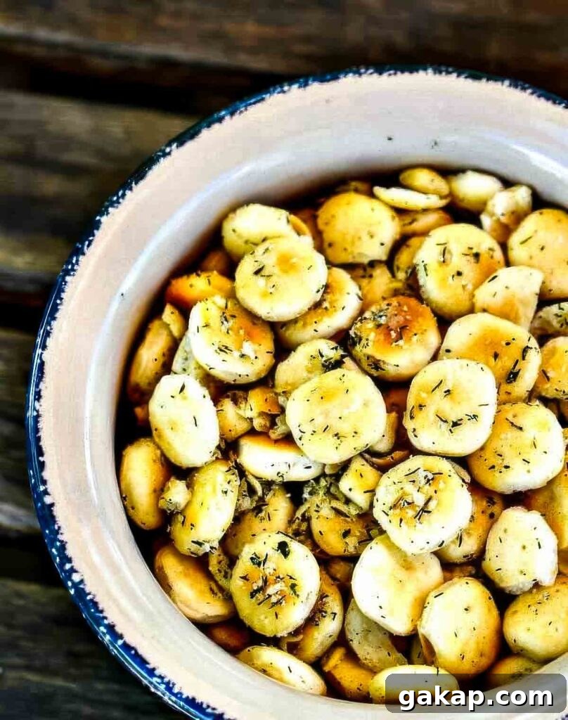 Top-down view of seasoned ranch oyster crackers in a white ceramic bowl with blue trim, resting on a wooden table.