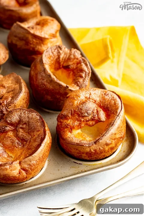 Yorkshire puddings in a Yorkshire pudding pan with a mustard yellow napkin and 2 forks in the background.