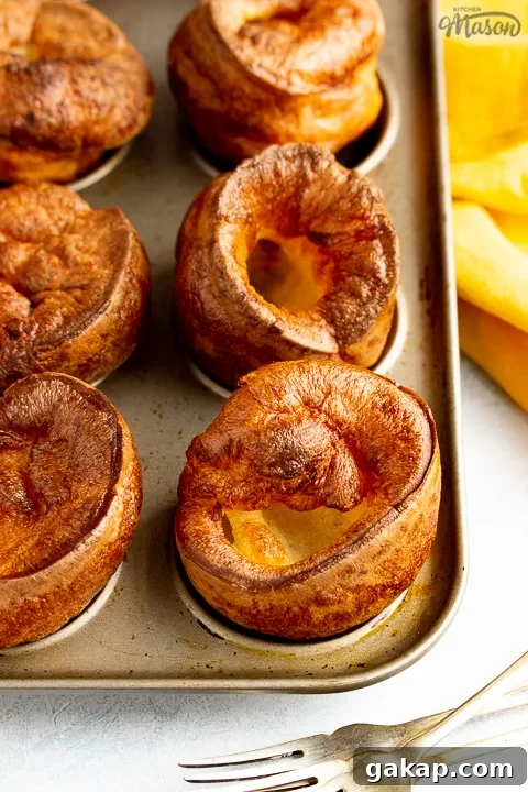 Yorkshire puddings in a Yorkshire pudding pan with a mustard yellow napkin and 3 forks in the background.