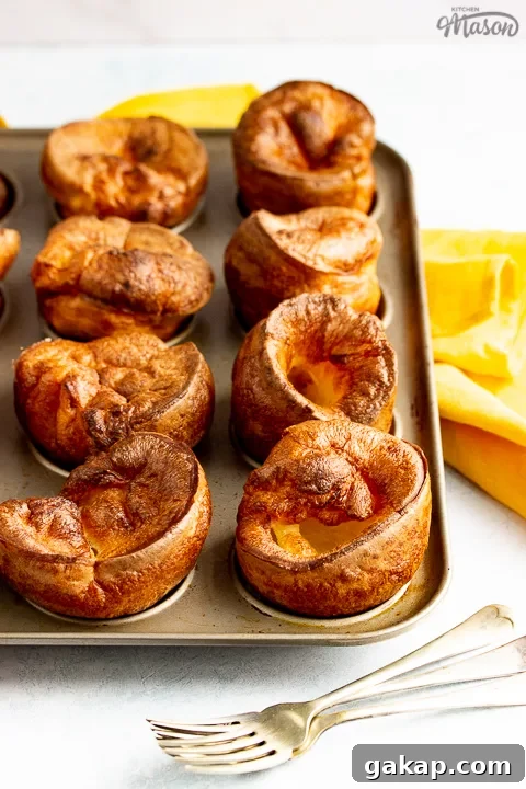 Yorkshire puddings in a Yorkshire pudding pan with a mustard yellow napkin and 3 forks in the background.