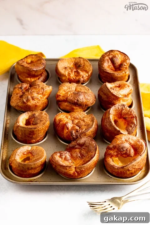Yorkshire puddings in a Yorkshire pudding pan with a mustard yellow napkin and 2 forks in the background.
