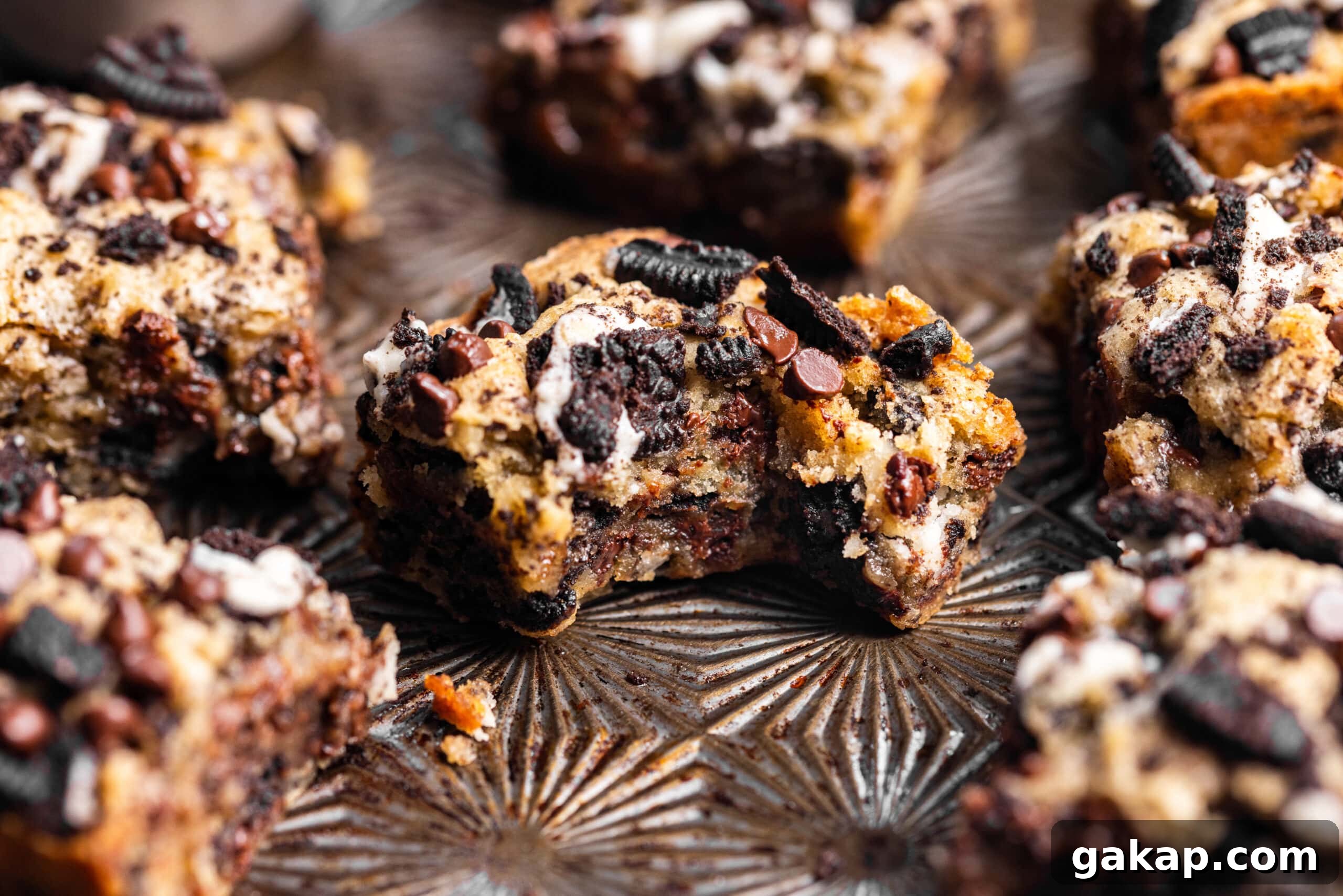 Oreo blondies on a baking sheet with a bite missing from one of them showing gooey texture.