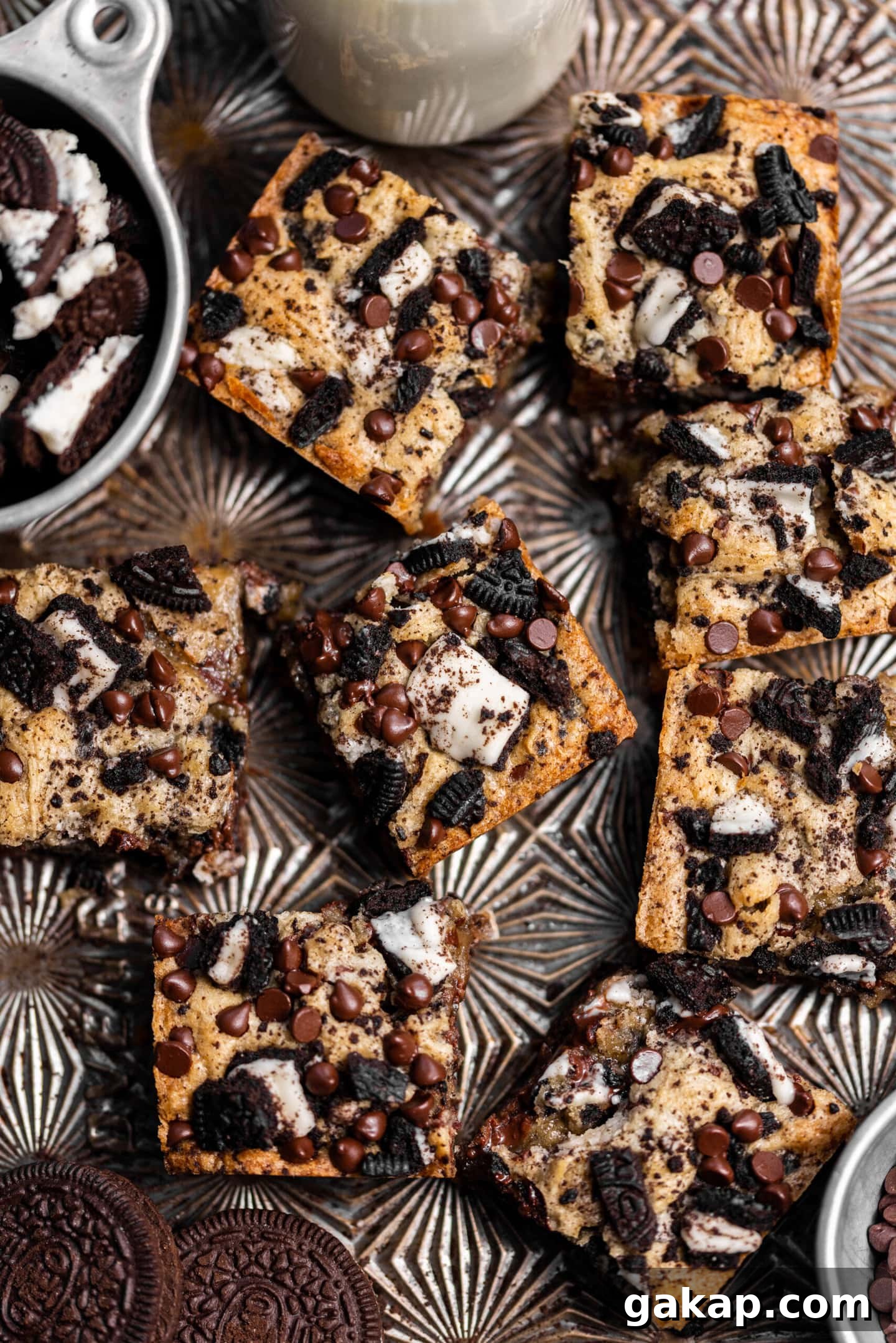 Oreo blondies spread on  a baking sheet next to chopped Oreos and a glass of milk.