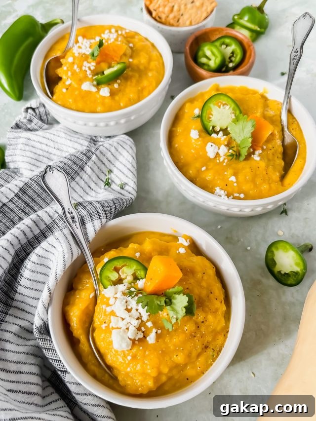 three bowls of butternut squash soup garnished with jalapeño and feta cheese with silver spoon inserted into each bowl.