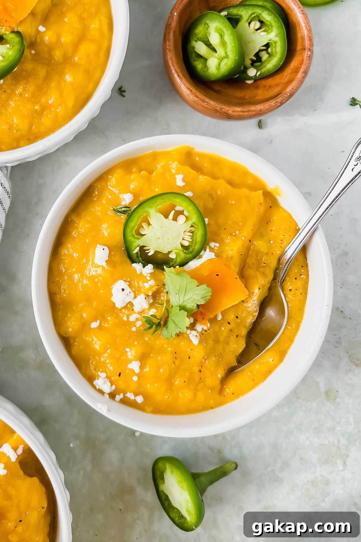 bowl of butternut squash soup garnished with jalapeño and feta cheese with silver spoon inserted into bowl.