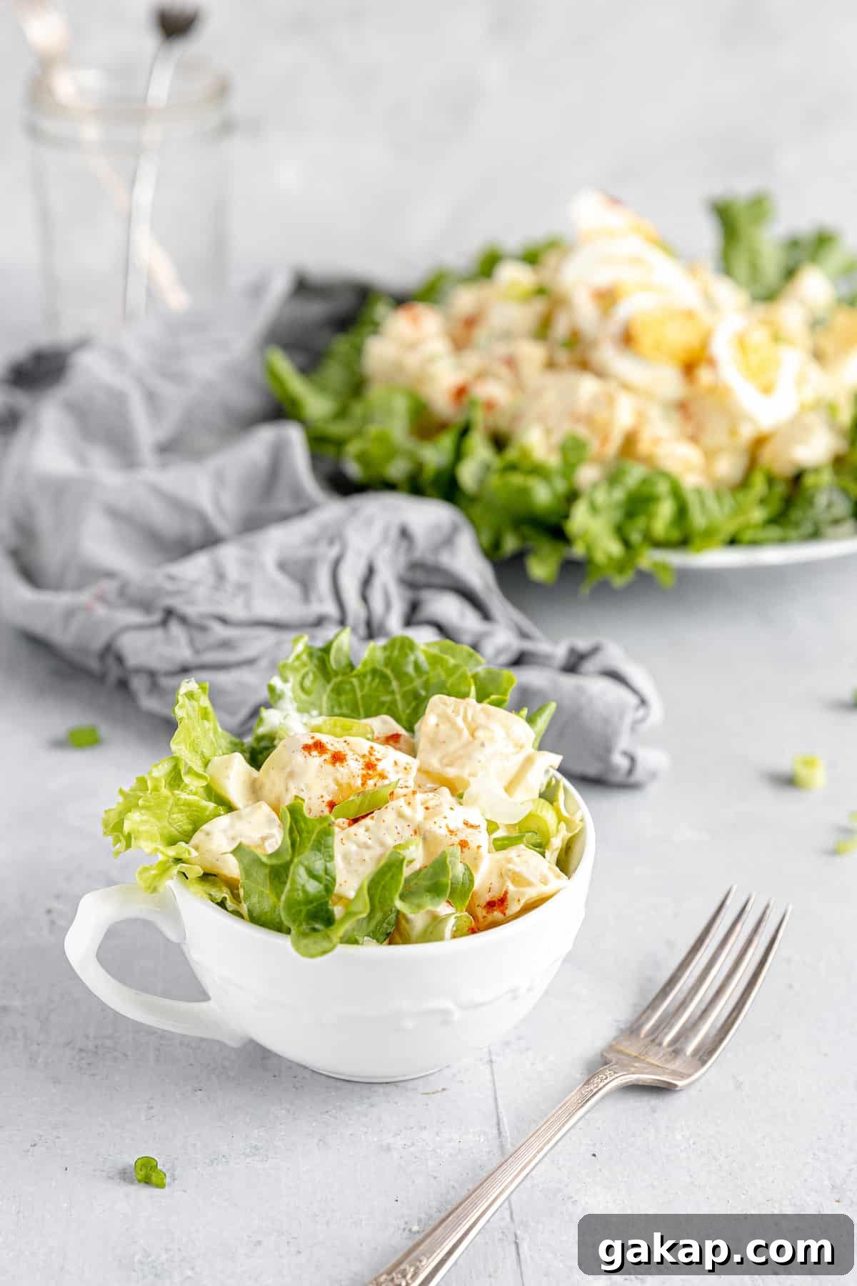 A Serving of Potato Salad in a Mug with the Remaining Salad on a Plate in the Background