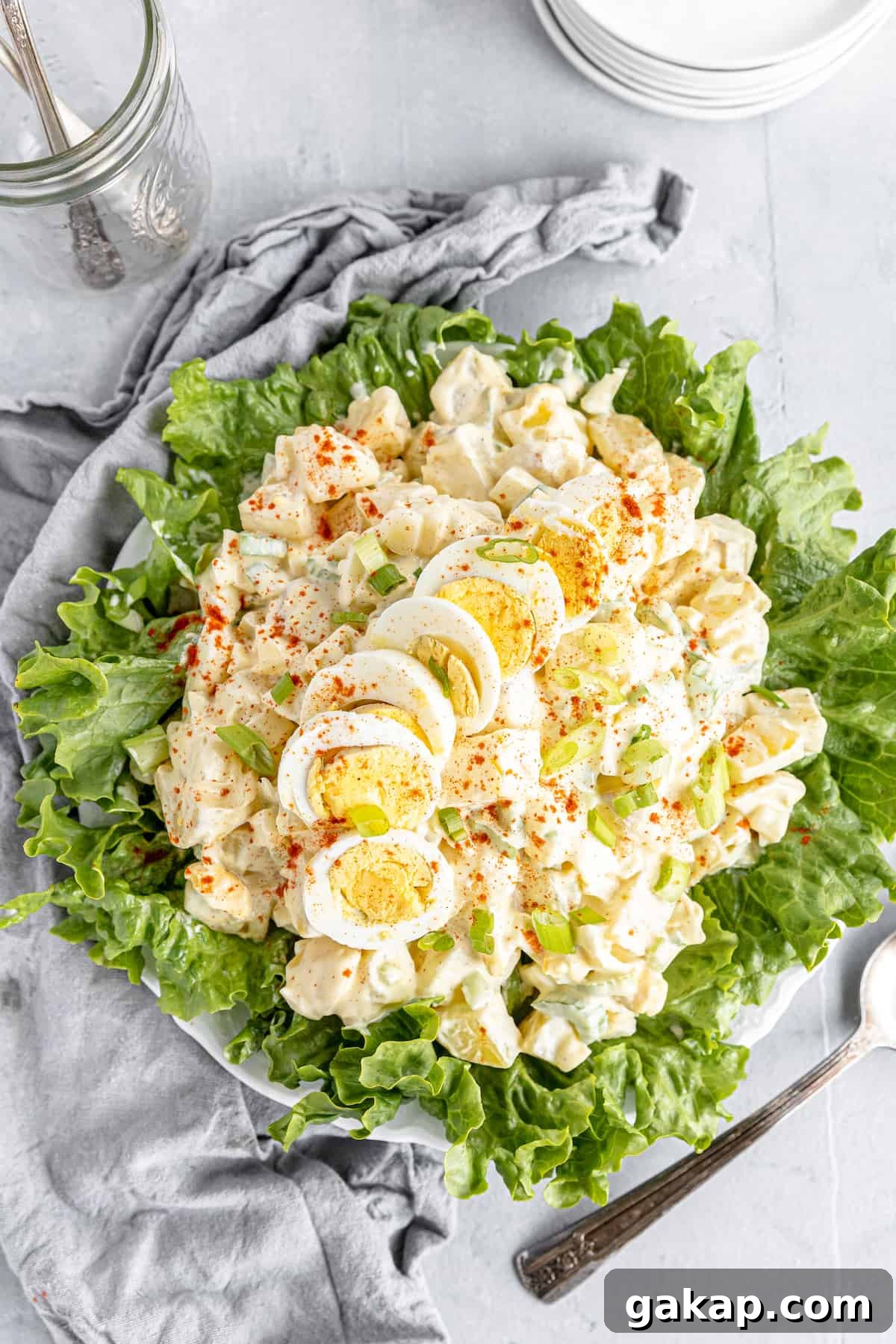 An Overhead Shot of a Potato Salad on a Lettuce-Lined Plate Beside a Gray Kitchen Towel