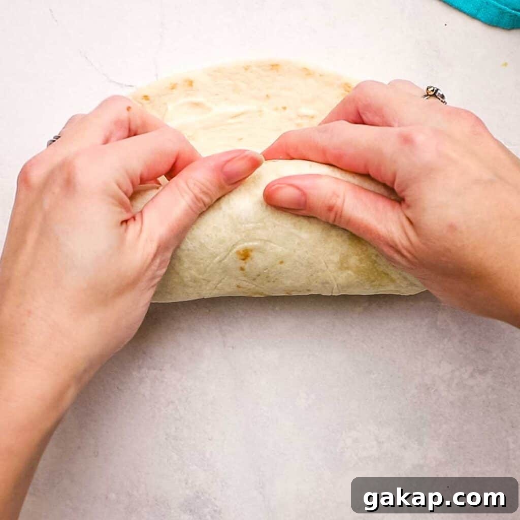 Rolling the tortilla wrap to make the ends meet and securing all the ingredients inside.