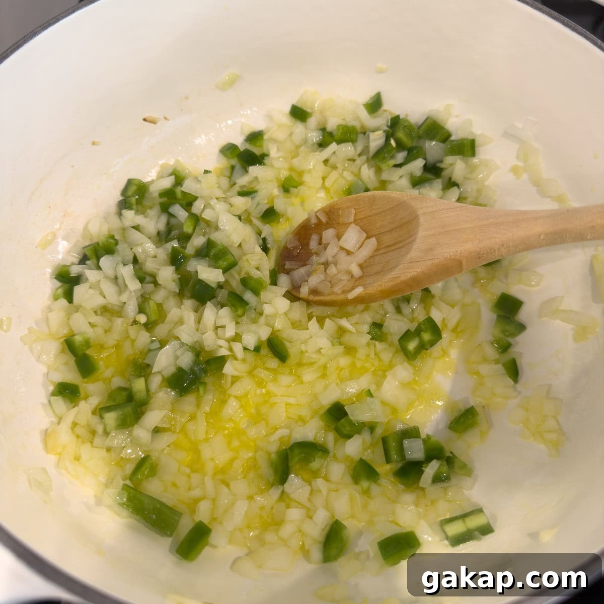 Chilies, onions, and oil cooking in olive oil in a white pot.