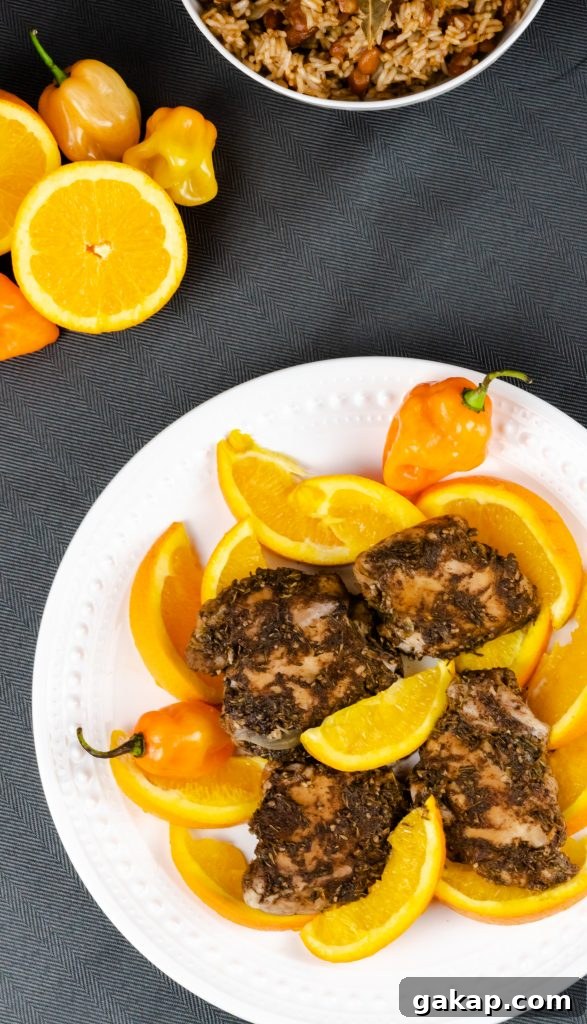 Top view of Jamaican Jerk chicken served on a platter with orange slices and hot peppers.